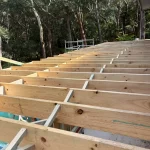 Installation of timber joists for a large deck, with metal bridging for stability, overlooking a dense forest.