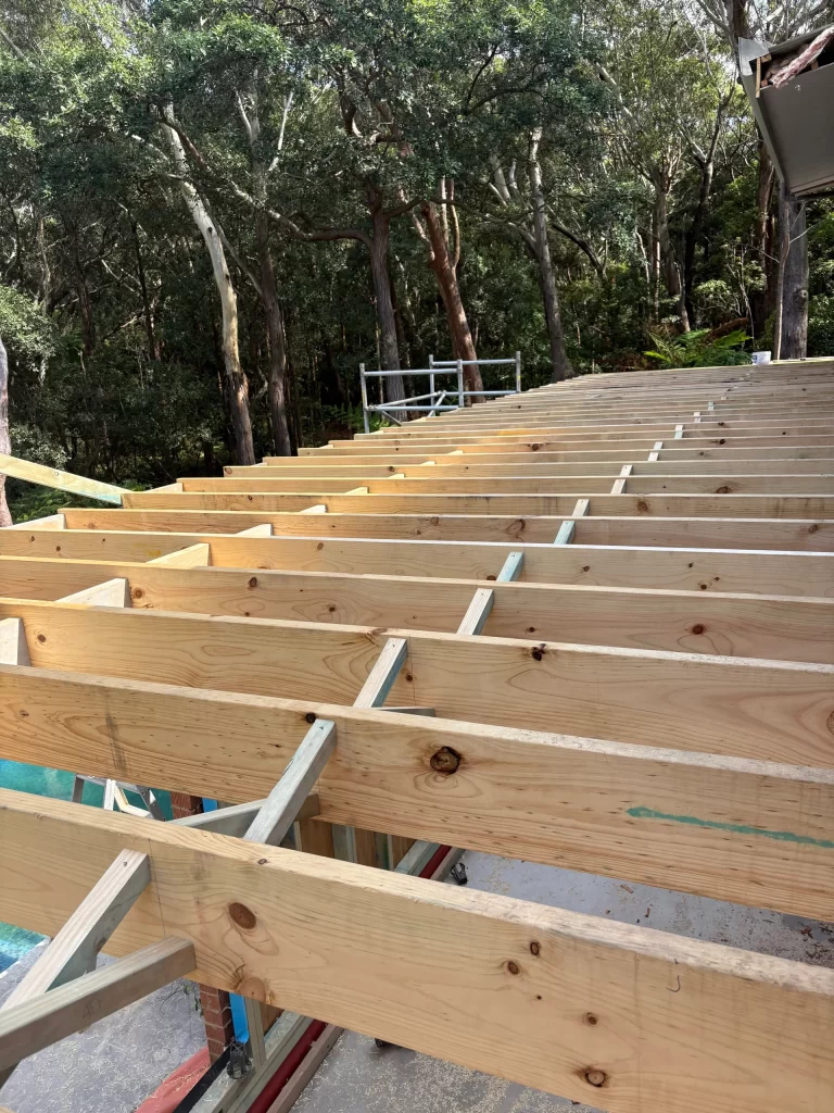 Installation of timber joists for a large deck, with metal bridging for stability, overlooking a dense forest.