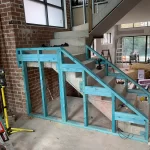 Installation of a blue-painted timber frame alongside a new concrete staircase, within a residential construction site.
